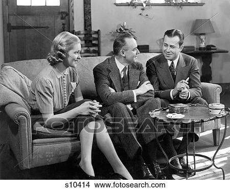 1930S 1940S Two Men And Woman Social Group Sitting On Couch Talking Indoor View Large Photo Image Picture - 1930S 1940S Two Men And Woman Social Group Sitting On Couch Talking Indoor. Fotosearch