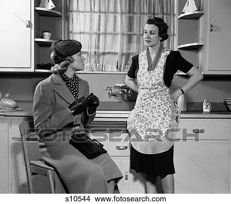 1930S 1940S Two Women Sitting In Kitchen Talking One Housewife Homemaker In Apron One In Coat And Hat Visiting Together Gossip View Large Photo Image Picture - 1930S 1940S Two Women Sitting In Kitchen Talking One Housewife Homemaker In Apron One In Coat And Hat Visiting Together Gossip. Fotosearch