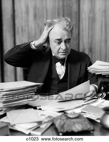 Stock Image - 1930S Elderly Businessman Sitting At Desk Among Stacks Of Papers With Hand In Hair & Flustered Expression. Fotosearch