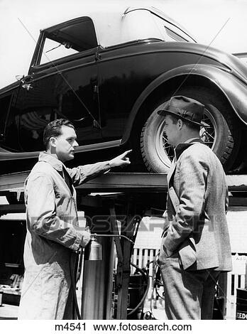 1930S Service Station Attendant In Coveralls Holding Oil Can Pointing At Problem Convertible On Lift Talking To Owner View Large Photo Image Stock Image - 1930S Service Station Attendant In Coveralls Holding Oil Can Pointing At Problem Convertible On Lift Talking To Owner. Fotosearch