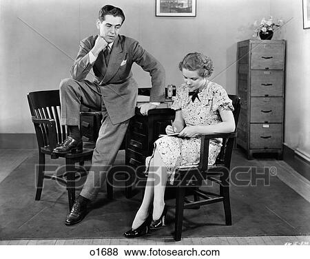 1940S Businessman Leaning Against Desk With Foot Propped On Chair Leering Ogling Secretary Sitting Next To Him Taking Notes View Large Photo Image Stock Photo - 1940S Businessman Leaning Against Desk With Foot Propped On Chair Leering Ogling Secretary Sitting Next To Him Taking Notes. Fotosearch
