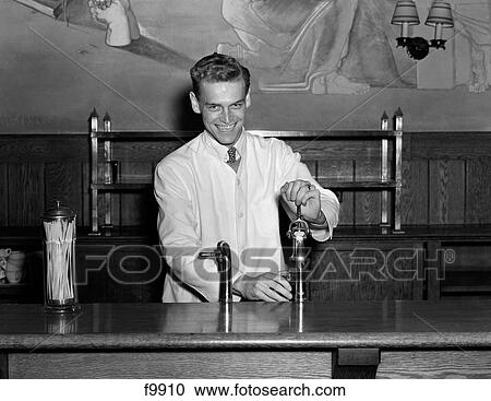 1940S Smiling Soda Jerk Dressed In Shirt Tie & White Smock Standing Behind Fountain Counter Filling Glass Looking At The Camera View Large Photo Image Stock Image - 1940S Smiling Soda Jerk Dressed In Shirt Tie & White Smock Standing Behind Fountain Counter Filling Glass Looking At The Camera. Fotosearch
