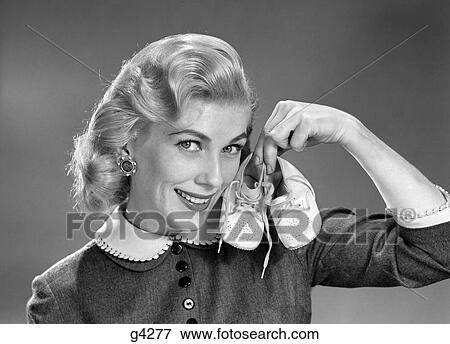 1950S 1960S Smiling Blond Woman Communicating That She Is Mother To Be By Holding Up A Pair Of Baby Shoes Looking At Camera View Large Photo Image Stock Photo - 1950S 1960S Smiling Blond Woman Communicating That She Is Mother To Be By Holding Up A Pair Of Baby Shoes Looking At Camera. Fotosearch