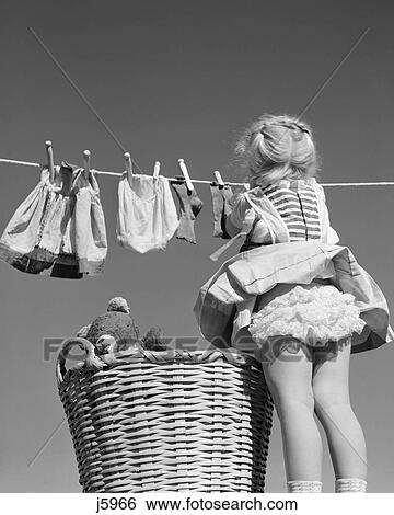 Stock Photograph - 1950S Back View Of Girl Hanging Laundry Wind Blowing Skirt To Show Ruffled Panties. Fotosearch