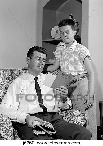 Stock Image - 1950S Boy Standing Looking Down At Father Reviewing His Report Card. Fotosearch