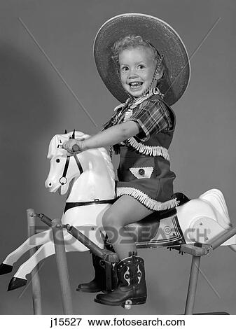 Stock Photo - 1950S Girl Dressed As Cowgirl Riding Rocking Horse. Fotosearch