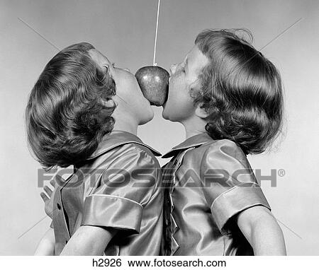 1950S Identical Twin Girls Trying To Eat An Apple Hanging In The Air From A String View Large Photo Image Stock Photograph - 1950S Identical Twin Girls Trying To Eat An Apple Hanging In The Air From A String . Fotosearch