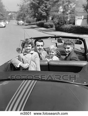 Stock Image - 1950S Portrait Well Dressed Family Mom Dad Son Daughter In Convertible Car Top Down Looking At Camera Over Back Of Trunk. Fotosearch