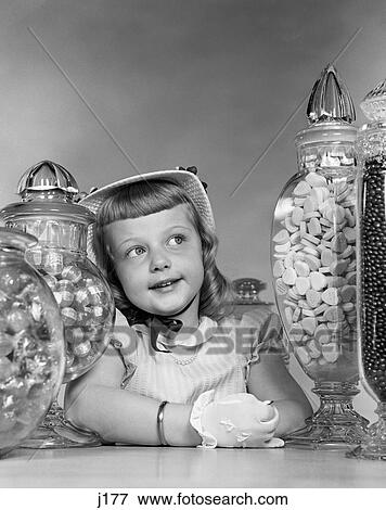Stock Photo - 1950S Smiling Girl With Bonnet And White Gloves Sandwiched Between Large Candy Jars On Counter . Fotosearch