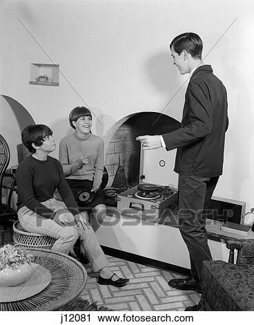 1960S 2 Teen Girls Seated On Wicker Stool At Fireplace Changing 45 Rpm Records With Teen Boy Dancing View Large Photo Image Stock Image - 1960S 2 Teen Girls Seated On Wicker Stool At Fireplace Changing 45 Rpm Records With Teen Boy Dancing. Fotosearch