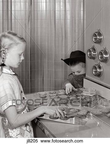 1960S Blond Girl Taking Cookies Off Tray At Kitchen Counter Younger Boy With Cowboy Hat Bandana Mask Reaches To Steal Them View Large Photo Image Stock Photography - 1960S Blond Girl Taking Cookies Off Tray At Kitchen Counter Younger Boy With Cowboy Hat Bandana Mask Reaches To Steal Them. Fotosearch