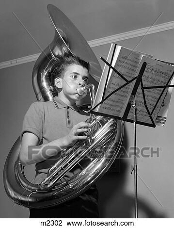 Stock Image - 1960S Boy Playing The Tuba While Reading From Sheet Music On A Music Stand Inside. Fotosearch
