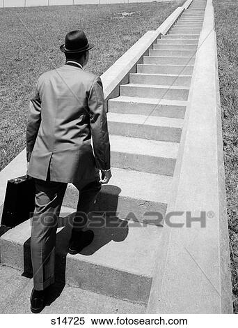 1960S Business Man In Suit & Fedora Holding Briefcase Starting Up Long Flight Of Cement Stairs Ahead Of Him View Large Photo Image Stock Photography - 1960S Business Man In Suit & Fedora Holding Briefcase Starting Up Long Flight Of Cement Stairs Ahead Of Him. Fotosearch