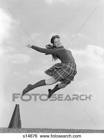 Stock Photograph - 1960S Cheerleader In Sweater Plaid Skirt & Knee Socks Leaping High In Air Looking At Camera. Fotosearch