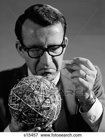Stock Photo - 1960S Close-Up Of Man In Suit & Glasses Pulling Strand Of Yarn From Large Ball Of Multi-Colored Pieces Tied Together. Fotosearch