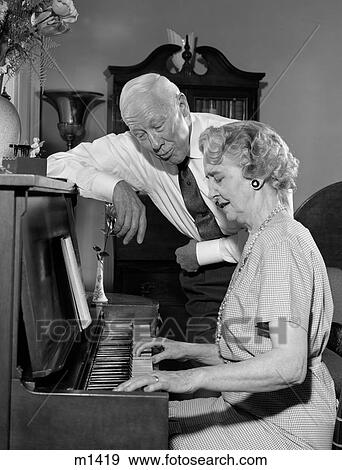 1960S Elderly Woman Playing Piano With Husband Standing Next To Her Singing View Large Photo Image Stock Photo - 1960S Elderly Woman Playing Piano With Husband Standing Next To Her Singing. Fotosearch