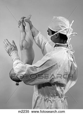 1960S Man Doctor Holding Newborn Baby Upside-Down By Ankles Slapping Bottom To Start It Breathing Stereotype Of Birth Process View Large Photo Image Stock Photography - 1960S Man Doctor Holding Newborn Baby Upside-Down By Ankles Slapping Bottom To Start It Breathing Stereotype Of Birth Process. Fotosearch