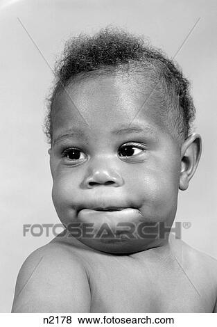 Stock Photo - 1960S Portrait Of African-American Baby Making A Funny Face Biting His Lip. Fotosearch