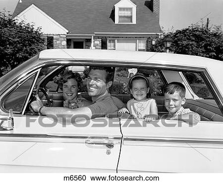 Stock Image - 1960S Smiling Family Father Mother Daughter Son Sitting In Car In Front Of Suburban House Side View Outside. Fotosearch