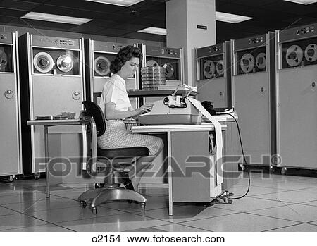 1960S Woman In Mainframe Computer Room Surrounded By Many Data Tape Drives Sitting At Desk Typing On Typewriter Indoor View Large Photo Image Picture - 1960S Woman In Mainframe Computer Room Surrounded By Many Data Tape Drives Sitting At Desk Typing On Typewriter Indoor. Fotosearch