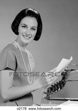 Stock Photo - 1960S Woman Secretary Smiling Seated At Desk With Manual Typewriter Looking At Camera. Fotosearch