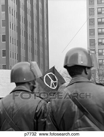1970S Back View Of Two Policeman In Helmets At Demonstration With Peace Sign In Background Framed Between Their Heads View Large Photo Image Stock Image - 1970S Back View Of Two Policeman In Helmets At Demonstration With Peace Sign In Background Framed Between Their Heads. Fotosearch