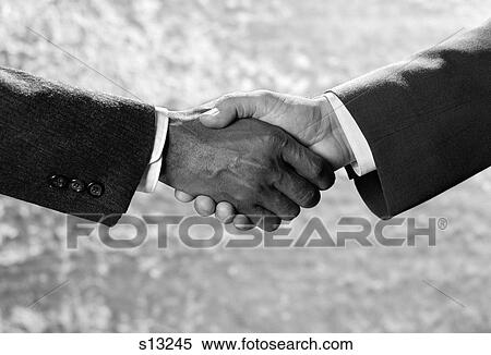 Stock Photography - 1970S Handshake Close-Up African-American And Caucasian Businessman Shaking Hands Studio Indoor. Fotosearch