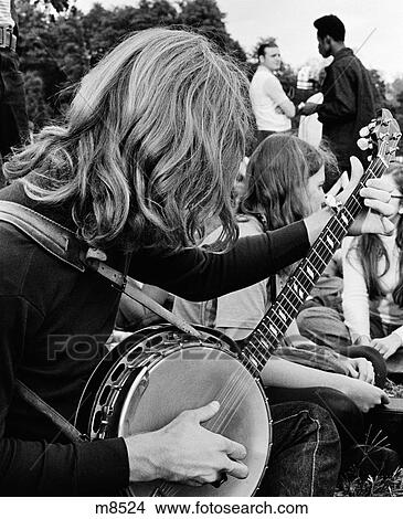 1970S Side View Of Hippie Teen Outdoor Gathering With Long-Haired Boy In Foreground Playing Banjo View Large Photo Image Picture - 1970S Side View Of Hippie Teen Outdoor Gathering With Long-Haired Boy In Foreground Playing Banjo. Fotosearch