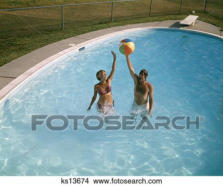 Picture - 1980 1980S Man Woman Couple Jumping Up Beach Ball Backyard Swimming Pool Men Women Couples Swim Pools Fun Summer . Fotosearch