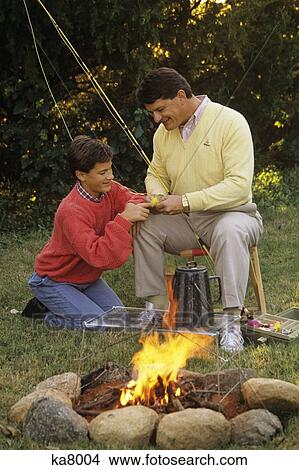 1990S Father And Son By Campfire Working On Fishing Rod And Flies View Large Photo Image Picture - 1990S Father And Son By Campfire Working On Fishing Rod And Flies. Fotosearch