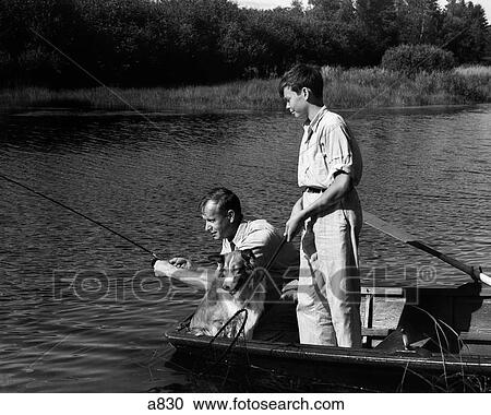 Stock Image - 1930S Man Father Teenage Boy Son Dog In Row Boat Fishing In Pond . Fotosearch