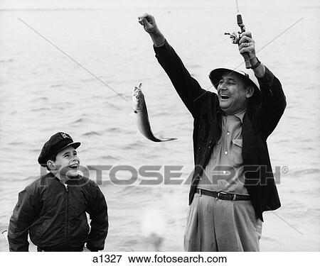 Stock Photo - 1950S 1960S Boy Son Fishing With Man Father Or Grandfather Holding Up Caught Fish On Line Laughing Having Fun . Fotosearch