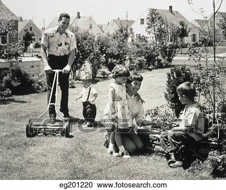 Stock Image - 1950S Family In Backyard Dad And Toddler Cutting Grass Mom And Kids Gardening. Fotosearch