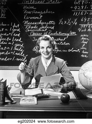 1950S Smiling Woman Elementary School Teacher Sitting Behind Desk In Front Of Blackboard Looking At Camera View Large Photo Image Picture - 1950S Smiling Woman Elementary School Teacher Sitting Behind Desk In Front Of Blackboard Looking At Camera. Fotosearch