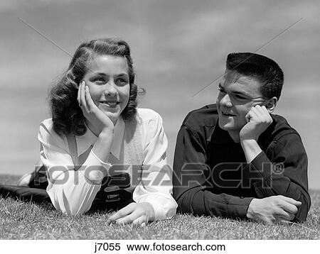 1950S Teenage Couple Laying On Grass Heads Propped On Hands Boy Gazing At Girl Wearing Cheerleader Sweater View Large Photo Image Stock Photography - 1950S Teenage Couple Laying On Grass Heads Propped On Hands Boy Gazing At Girl Wearing Cheerleader Sweater. Fotosearch