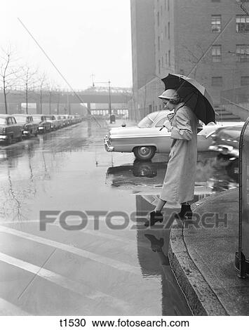 1950S Woman In Rain Coat Hat Boots Holding Umbrella Crossing City Street In Wet Foul Weather View Large Photo Image Stock Image - 1950S Woman In Rain Coat Hat Boots Holding Umbrella Crossing City Street In Wet Foul Weather. Fotosearch