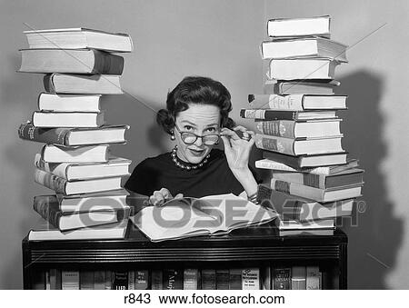Stock Image - 1950S Woman Sitting Between Stacks Of Books Pulling Down Glasses To Look Over Rims. Fotosearch