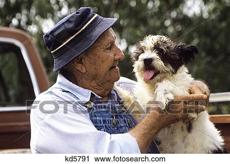 1990S Older Man Wearing Hat And Overalls Holding Dog View Large Photo Image Stock Image - 1990S Older Man Wearing Hat And Overalls Holding Dog. Fotosearch