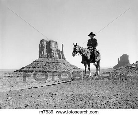 Stock Photo - Navajo Indian In Cowboy Hat On Horseback With Monument Valley Rock Formations In Background. Fotosearch