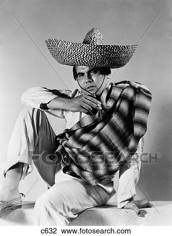 Stock Image - 1930S 1940S Stereotype Portrait Mexican Man Wearing Striped Serape Sombrero Hat Smoking Cigarette. Fotosearch