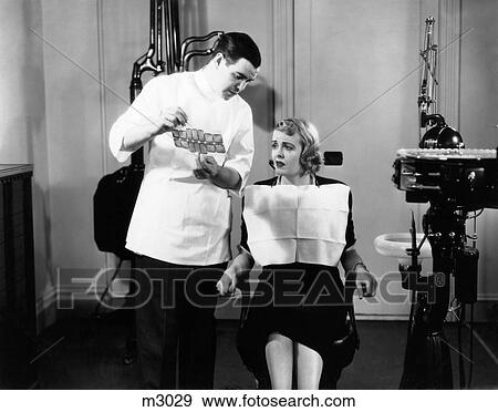 1930S Dentist Man Shows X-Rays To Woman Patient Sitting In Chair Wearing Bib View Large Photo Image Stock Photo - 1930S Dentist Man Shows X-Rays To Woman Patient Sitting In Chair Wearing Bib. Fotosearch