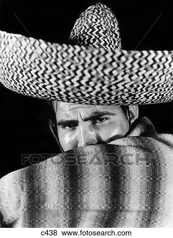 Stock Photo - 1930S Stereotype Portrait Mexican Man Wearing Sombrero Hat Striped Blanket Poncho Covering Mouth With Arm . Fotosearch