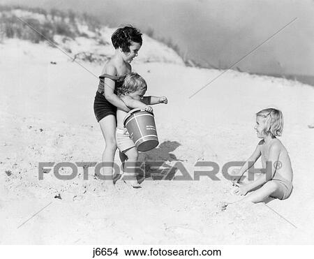 1930S Three Children Playing In Sand Beach Dunes Girls Toddler Bucket Summer Fun Seashore View Large Photo Image Picture - 1930S Three Children Playing In Sand Beach Dunes Girls Toddler Bucket Summer Fun Seashore . Fotosearch