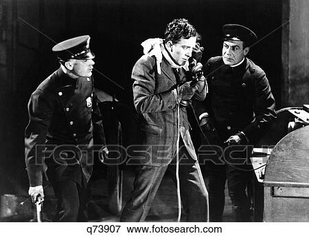 Stock Photo - 1930S Two Armed Police Looking At Anxious Desperate Man Robbery Victim Talking On Telephone. Fotosearch