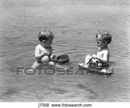 1930S Two Boys Toddlers Playing Sitting In Water Ocean With Sand Bucket Toy Boat View Large Photo Image Stock Photo - 1930S Two Boys Toddlers Playing Sitting In Water Ocean With Sand Bucket Toy Boat. Fotosearch