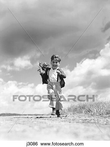 Stock Photograph - 1940S 1950S Boy Running Towards Camera On Country Road Holding Bouquet Of Spring Flowers In One Hand . Fotosearch