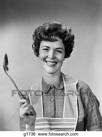 Stock Photograph - 1950S 1960S Portrait Smiling Woman Housewife Wearing Apron Holding Large Spoon . Fotosearch