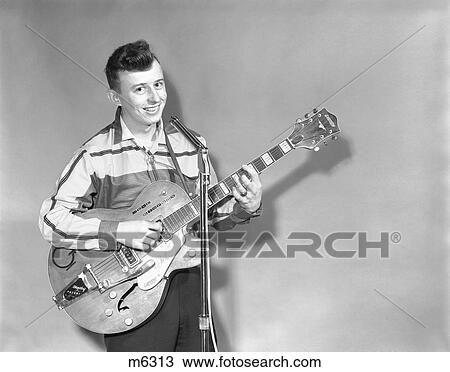 Stock Image - 1950S Teenage Boy Singing Playing Guitar Into Microphone. Fotosearch