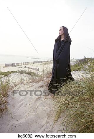 1960S 1970S Sad Gloomy Lone Woman Wearing Black Long Victorian Cape Standing On Beach Sand Dune View Large Photo Image Stock Image - 1960S 1970S Sad Gloomy Lone Woman Wearing Black Long Victorian Cape Standing On Beach Sand Dune. Fotosearch
