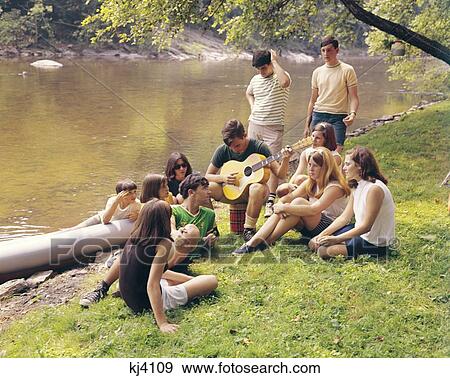 1960S Group Of Teenagers By Stream Listening To Boy Play The Guitar View Large Photo Image Stock Photo - 1960S Group Of Teenagers By Stream Listening To Boy Play The Guitar . Fotosearch